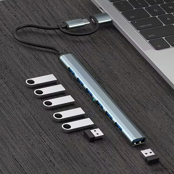 Ein grauer USB-C-Hub mit mehreren Anschlüssen ist an einen Laptop angeschlossen. Mehrere USB-Sticks liegen daneben.