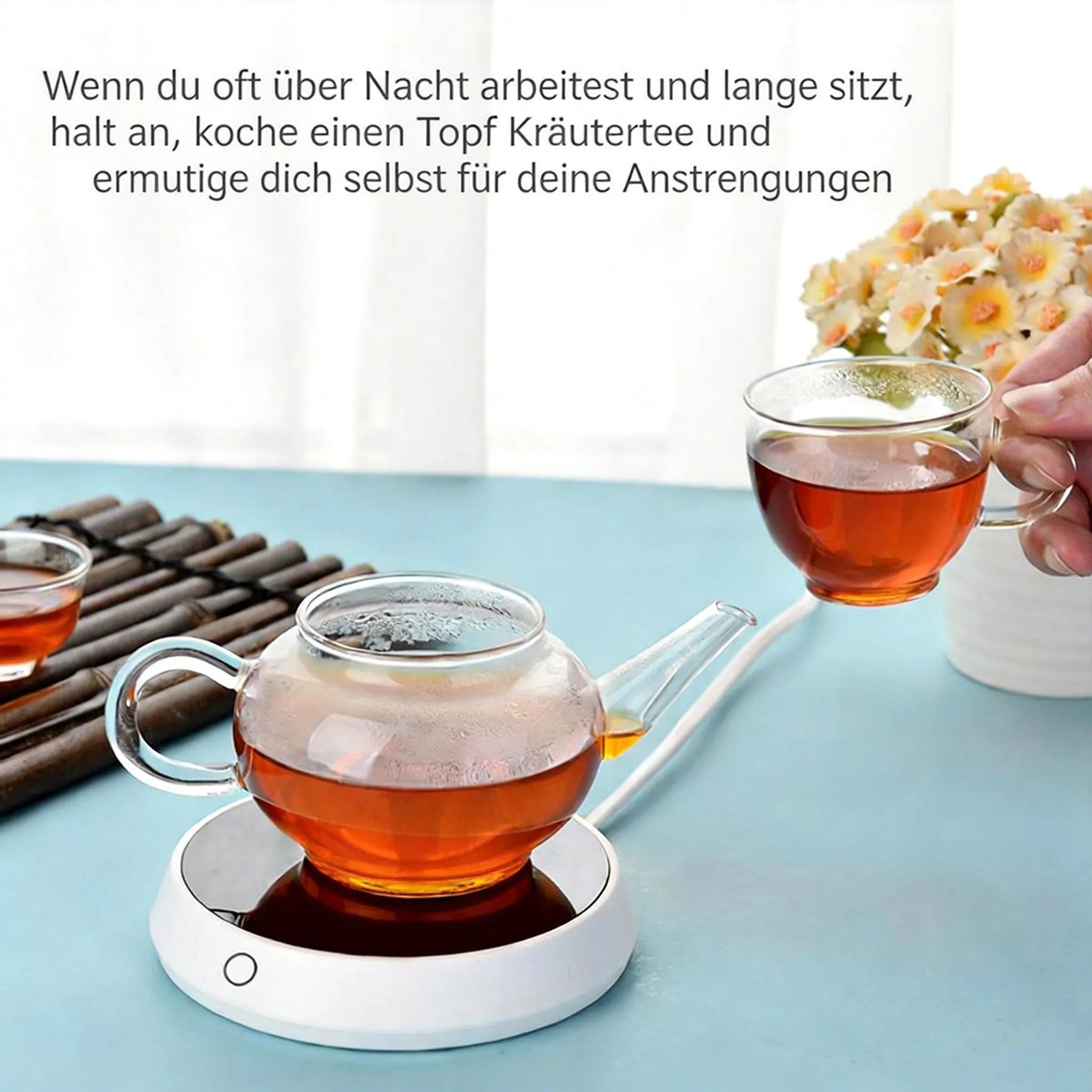 Ein Glas-Teekanne mit Tee auf einer weißen Heizplatte, daneben eine Tasse.