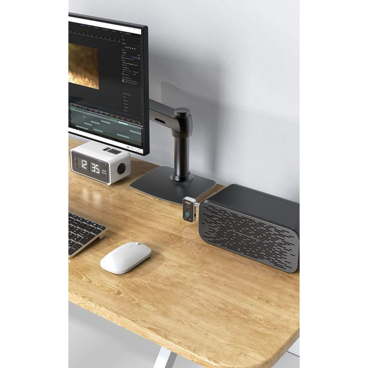 Schreibtisch mit Monitor, Tastatur, Maus, Uhr und Lautsprecher.