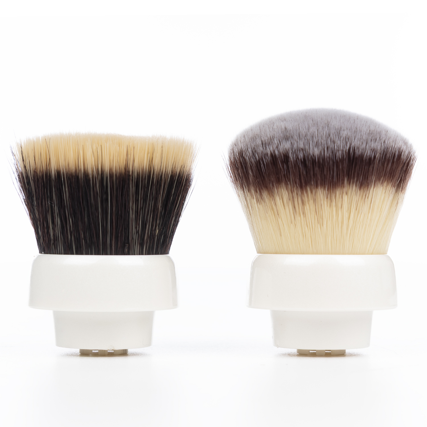 Due pennelli da trucco con manici bianchi e setole bicolori su sfondo bianco.