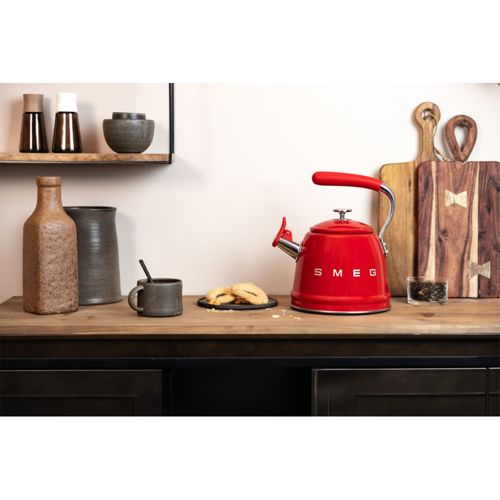 Un bollitore SMEG rosso siede su un bancone di legno con biscotti e una tazza accanto.