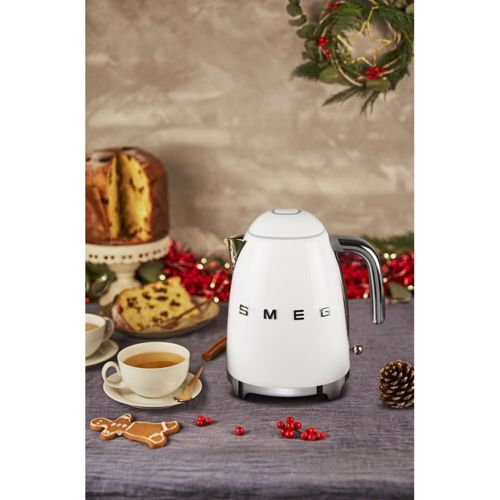 Ein weißer Smeg-Wasserkocher steht auf einem Tisch mit Panettone, Keksen und Tee.