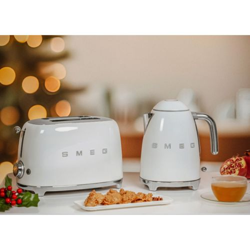 Ein weißer Smeg-Toaster und Wasserkocher stehen neben einem Teller mit Keksen und Granatapfel.