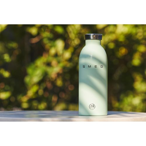 Eine hellgrüne Smeg-Wasserflasche mit silbernem Verschluss steht draußen auf einem Tisch.