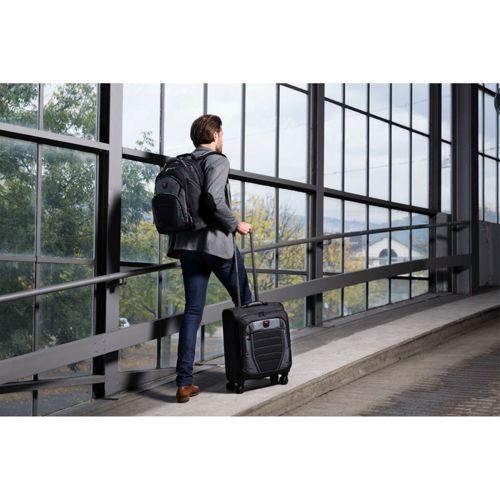 Un homme avec un sac à dos et une valise monte une rampe à côté de grandes fenêtres.