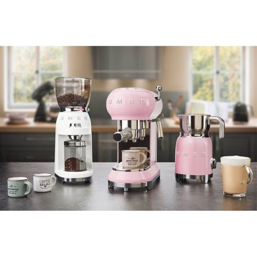 Trois machines à café et moulins Smeg roses et blancs sur un comptoir.
