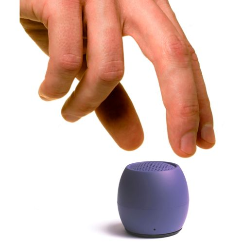 Eine Hand schwebt über einem kleinen, violetten, ovalen Lautsprecher mit perforierter Oberseite.