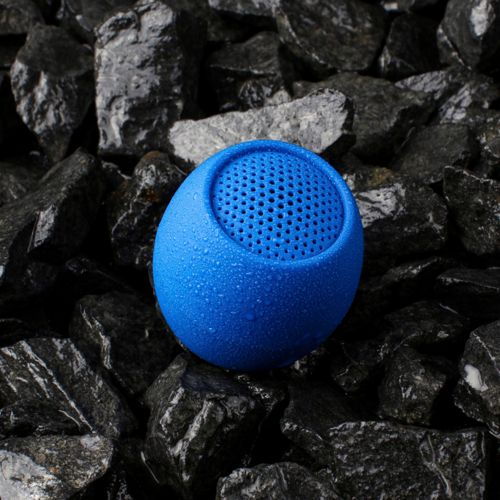 Een blauwe, met water bespikkelde luidspreker rust op donkere stenen.