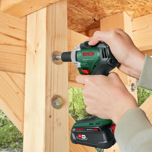 Hände benutzen eine Bosch-Bohrmaschine, um eine Schraube in einen Holzbalken zu schrauben. Eine weitere Schraube ist sichtbar.
