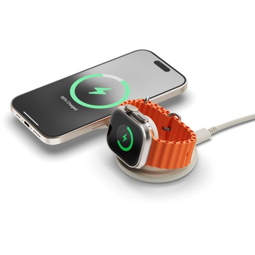 Eine silberne Apple Watch mit orangefarbenem Armband lädt auf einem weißen Ständer neben einem Telefon.