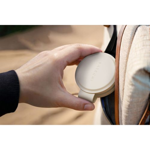 Eine Hand hält ein cremefarbenes, rundes Satechi-Gerät neben einer Tasche.