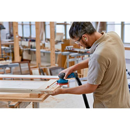 Mann schleift Holz mit Exzenterschleifer in Werkstatt.