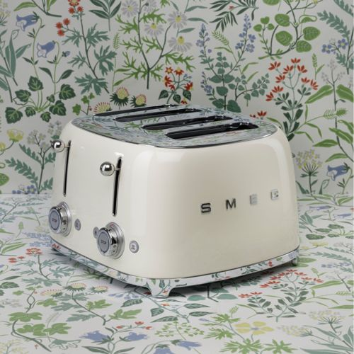 Krem rengi SMEG tost makinesi, krom detaylarla çiçek desenli bir yüzeyde duruyor.