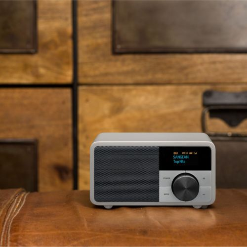 Una radio grigia con griglia dell'altoparlante nera e display è su un tavolo di legno.