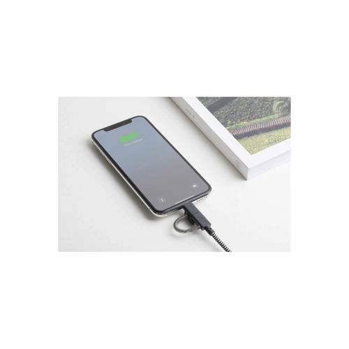 Uno smartphone si carica con un cavo, accanto a un libro su superficie bianca.