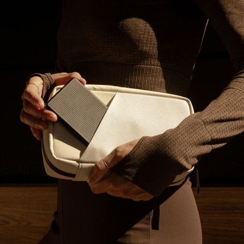 Une personne insère un objet gris perforé dans un sac couleur crème.