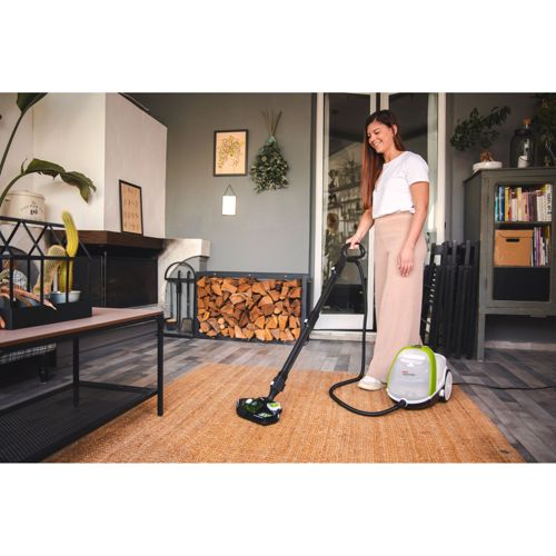 Eine Frau reinigt einen Teppich mit einem Dampfreiniger in einem Raum mit Kamin und Holz.