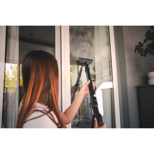 Eine Frau reinigt ein Fenster mit einem Dampfreiniger. Dampf steigt auf.