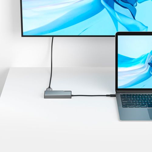 Un hub grigio collega un laptop a un grande monitor che visualizza un'immagine astratta blu.