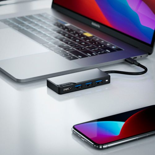 Un laptop con hub USB-C e uno smartphone su una scrivania bianca.