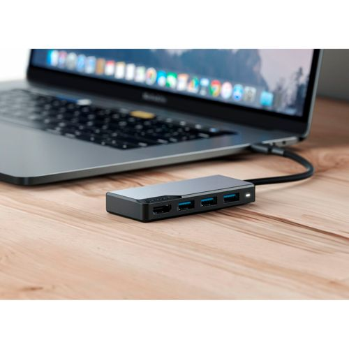 Un hub USB-C nero con porte HDMI e USB su una scrivania di legno accanto a un laptop.