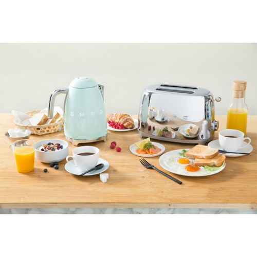 Ein Frühstückstisch mit einem mintgrünen Wasserkocher, Toaster, Kaffee, Saft und Gebäck.