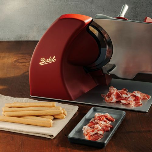 Rote Berkel-Aufschnittmaschine mit Brotstangen und Aufschnitt auf Holztisch.