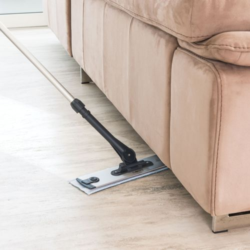 Un mocio pulisce il pavimento sotto un divano beige.