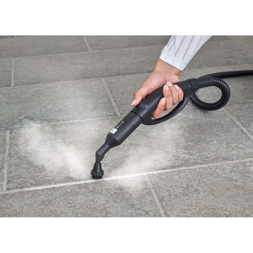 Une main tient un nettoyeur vapeur noir nettoyant des carreaux gris.