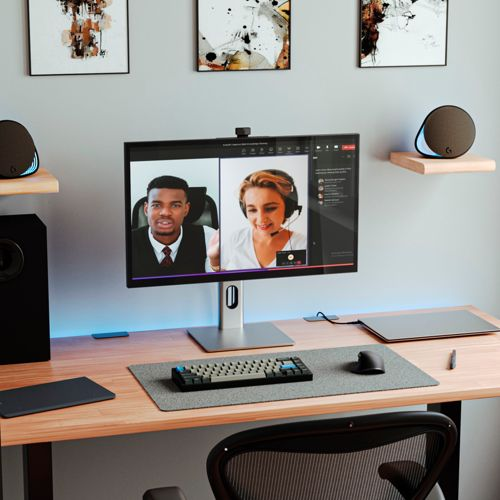 Scrivania con monitor per videoconferenze, tastiera, mouse, altoparlanti e arte murale.