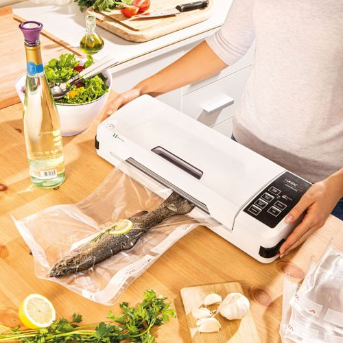 A person vacuum seals a fish in a plastic bag on a wooden table.