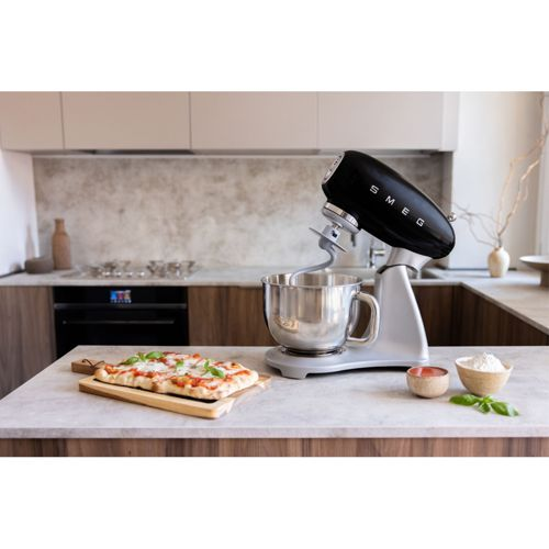 Una batidora de pie Smeg negra está sobre una encimera de cocina junto a una pizza.