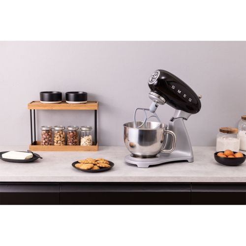 Un robot amasador SMEG negro con base plateada está en una encimera con frascos de nueces.