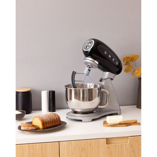 Un robot de cocina SMEG negro está en un mostrador con pan y mantequilla.