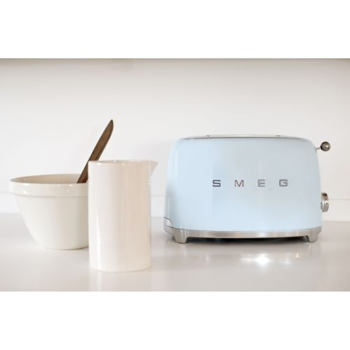 Ein hellblauer Smeg-Toaster steht neben einer weißen Kanne und einer Schüssel mit Holzlöffel.