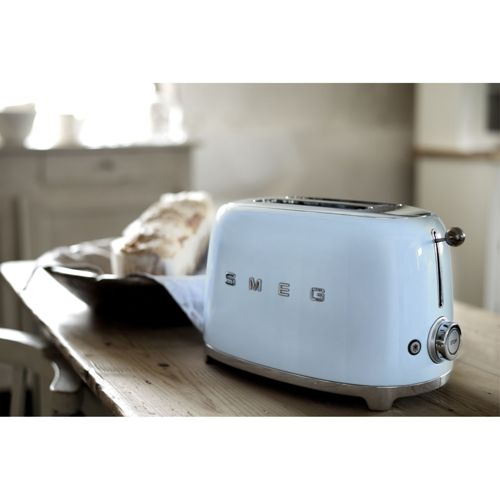 Ein hellblauer Smeg-Toaster steht auf einem Holztisch neben einem Laib Brot.