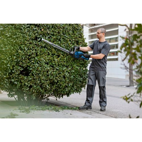 Mann trimmt eine grüne Hecke mit einem blau-schwarzen Heckenschneider im Freien.