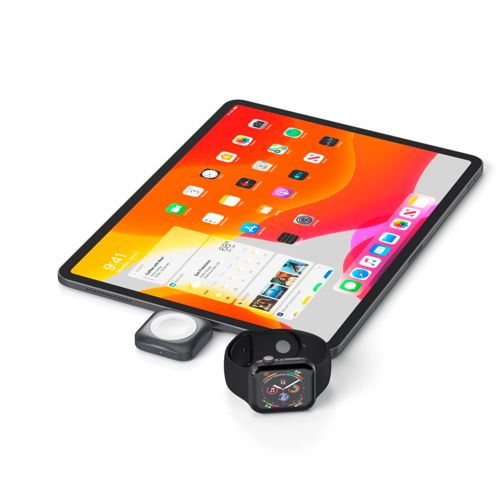 Apple Watch nera e caricabatterie su un tablet con schermata home colorata.