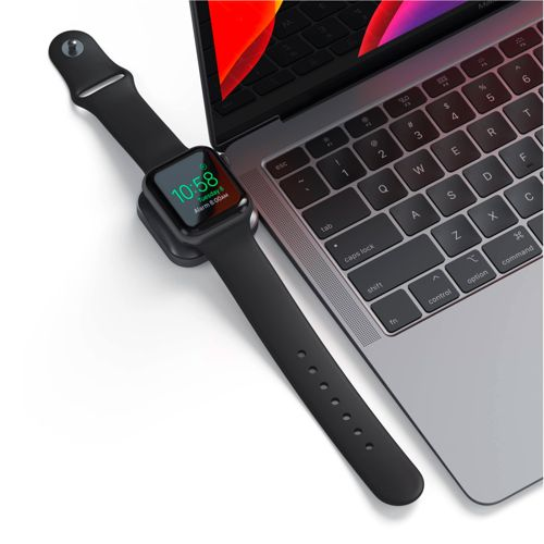 Uno smartwatch nero con cavo di ricarica accanto alla tastiera di un laptop.