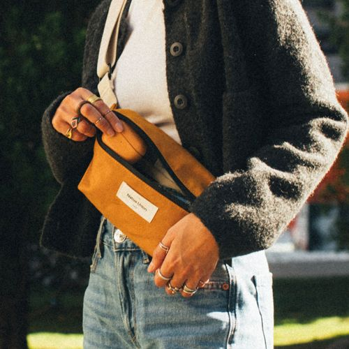 Persona in jeans e giacca tiene aperta una pochette gialla con etichetta bianca.