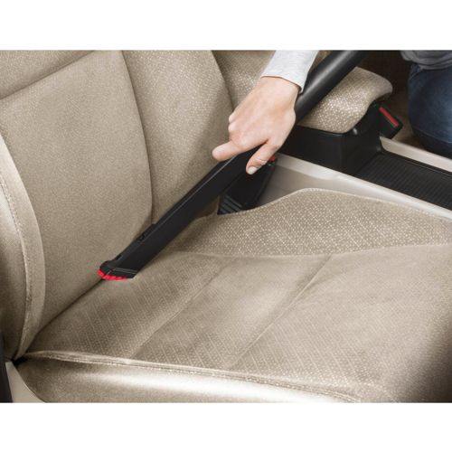 Una mano usa un accessorio nero per aspirapolvere per pulire un sedile auto beige.