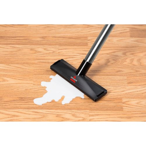 La testina di un aspirapolvere pulisce un liquido bianco versato su un pavimento in legno.
