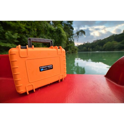 Orange Outdoor-Koffer auf einem roten Boot auf einem See mit Bäumen und bewölktem Himmel.