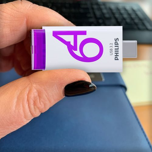 Ein Finger hält einen weißen USB-3.2-Stick mit lila Logo und Philips-Schriftzug.