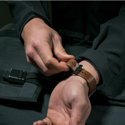 Eine Person schließt das Lederarmband einer braunen Armbanduhr am Handgelenk.