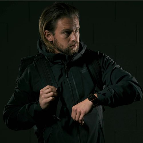 Ein Mann mit langen Haaren und Bart trägt eine dunkle Jacke und einen Rucksack.