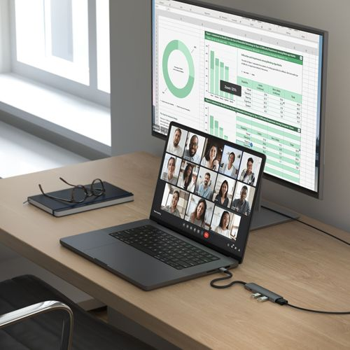 Un portátil muestra una videollamada, junto a un monitor grande con hojas de cálculo.