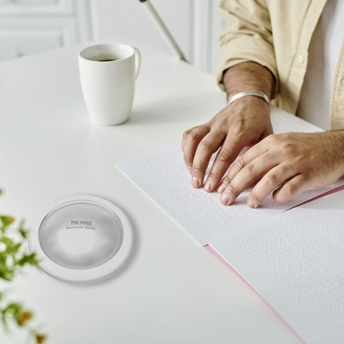 Eine Person liest Brailleschrift auf einem weißen Tisch mit einer Tasse Kaffee.