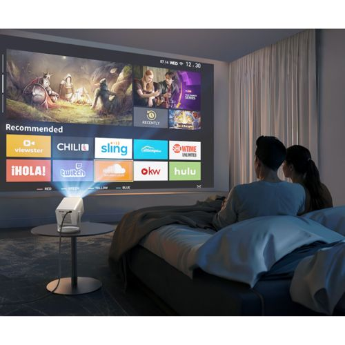 Ein Paar schaut auf einem Bett einen Film, der von einem Projektor auf eine Leinwand projiziert wird.