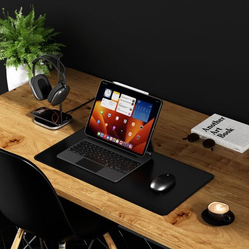Een houten bureau met een tablet, toetsenbord, muis, koptelefoon, plant en boek.
